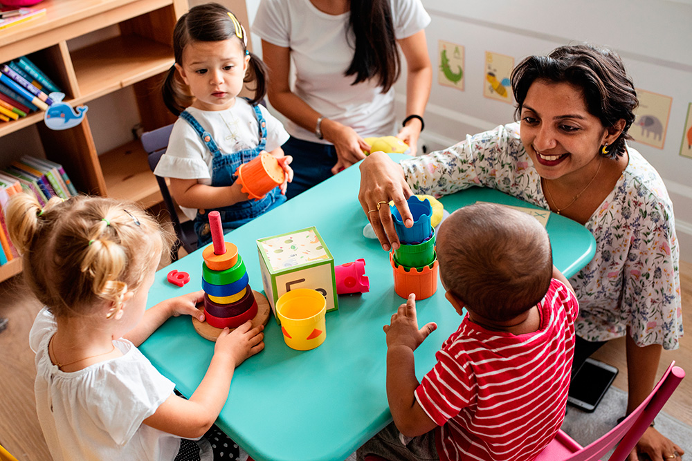 A teacher and children joyfully playing with toys in a bright, engaging classroom setting.