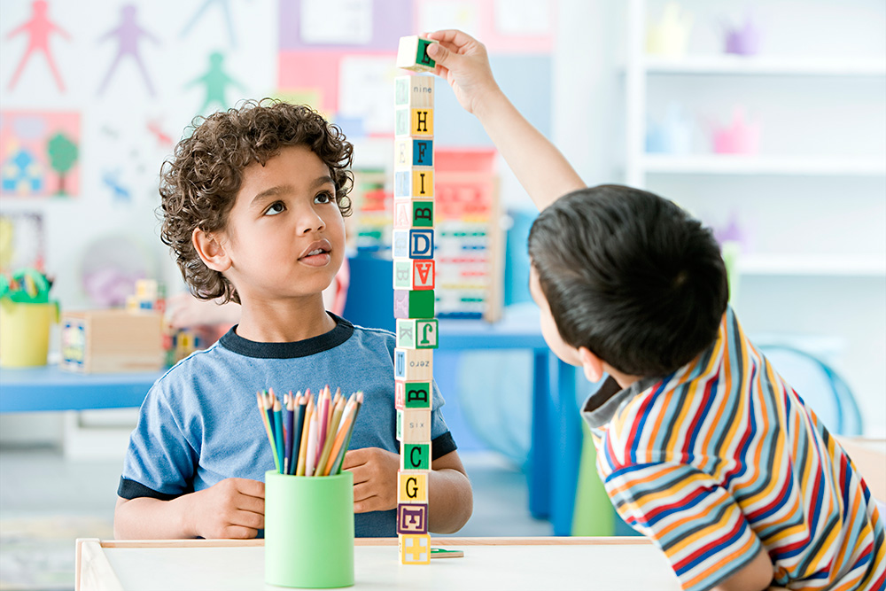 Two children engaged in play, building structures with colorful blocks in a bright classroom setting.