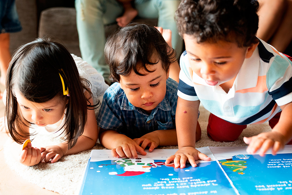 Three young children gathered around a book, engaged in reading, sharing smiles and enjoying the story.