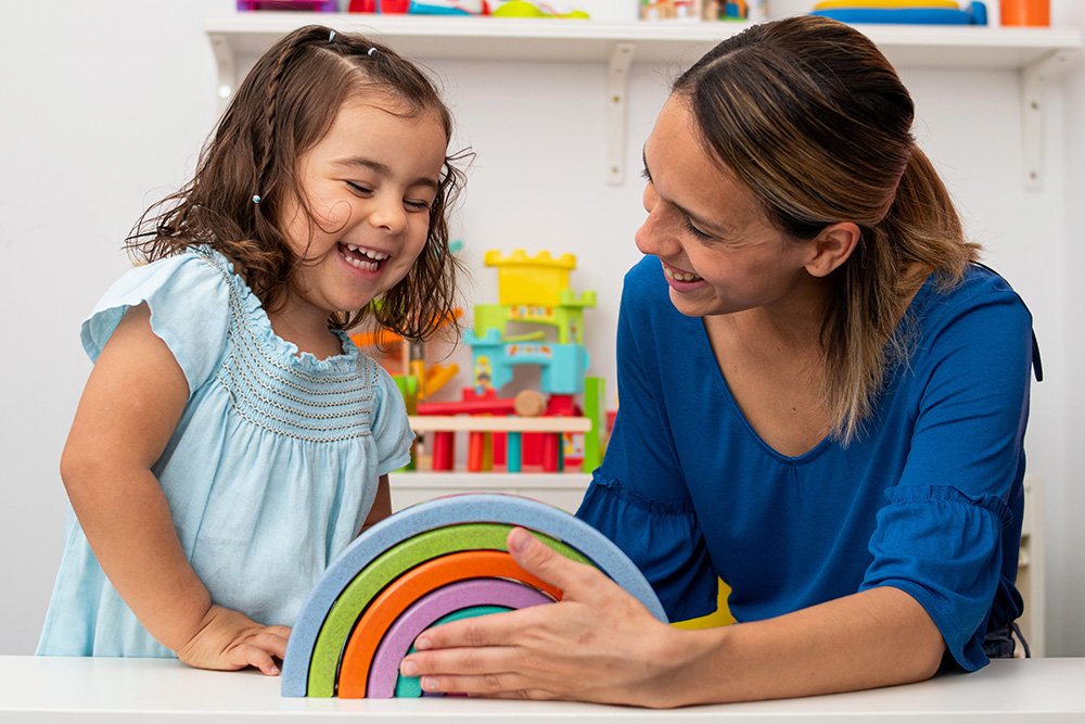 A teacher and a young girl joyfully playing together with a vibrant, rainbow-colored toy.