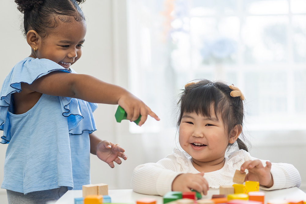 Two young girls happily constructing with wooden blocks, showcasing creativity and teamwork in their playtime activity.