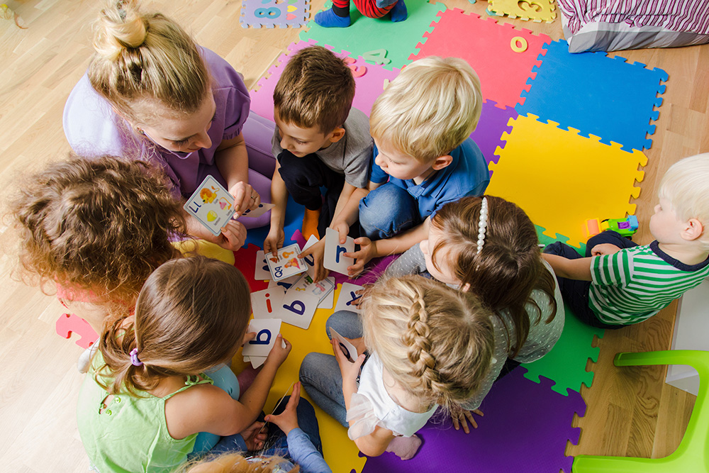 A group of preschool children engage in learning letters of the alphabet through the use of flash cards presented by their teacher.