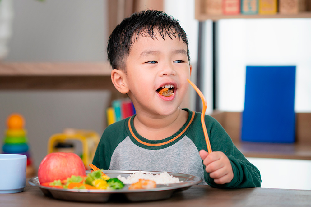 A young boy happily eats a nutritious meal with a fork, showcasing his enjoyment of healthy food.