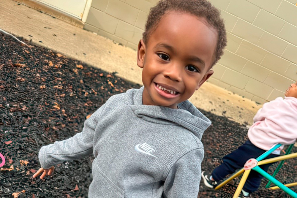 A young boy smiles joyfully while standing in a playground, engaging in outdoor learning activities.