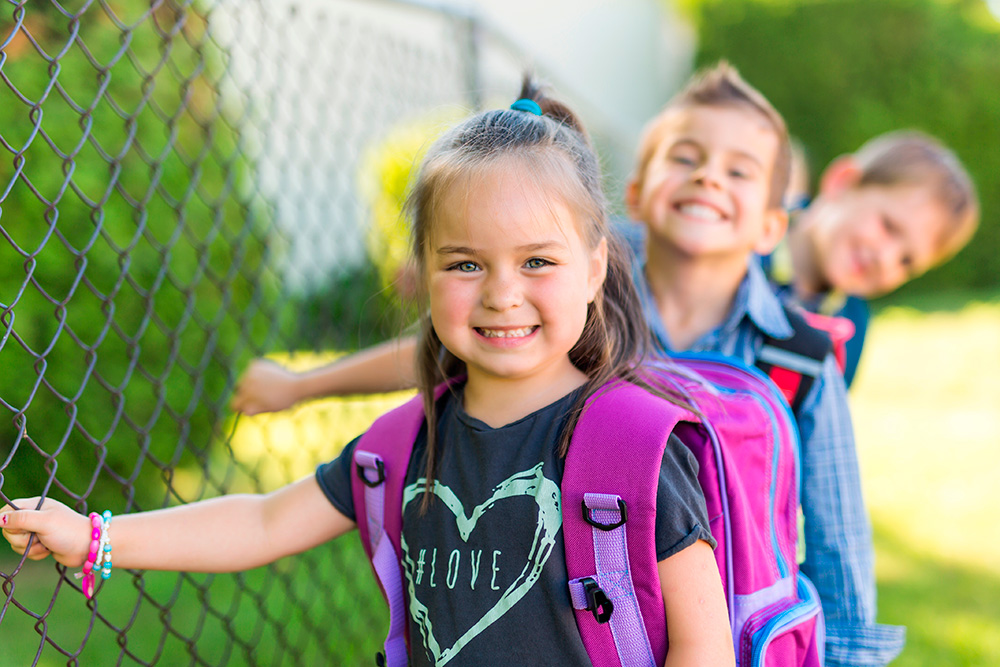 Three children with backpacks are positioned in front of a fence, emphasizing safety and readiness for their journey.