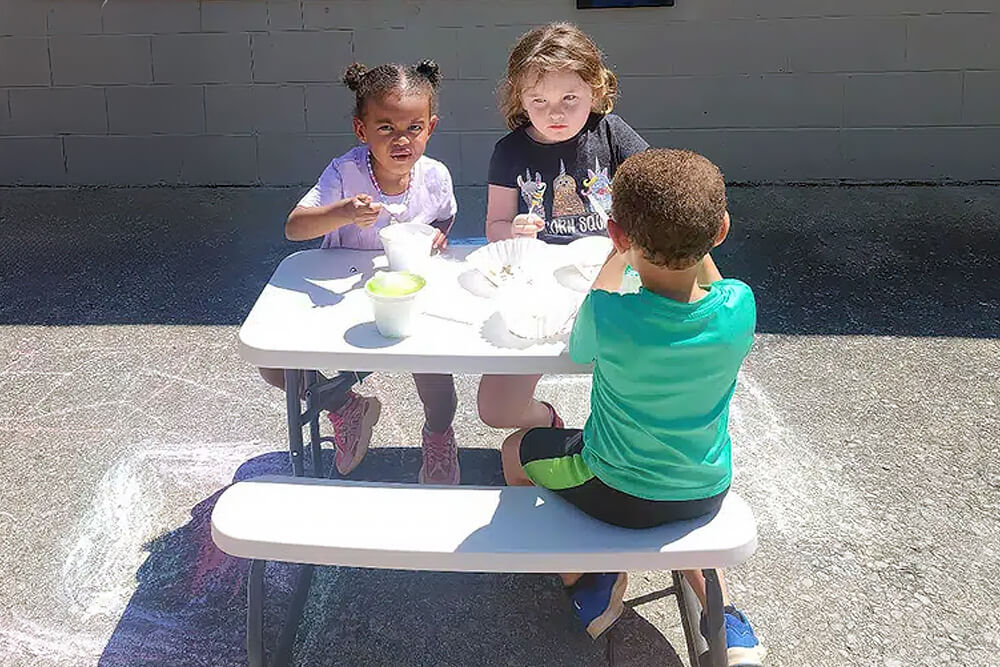 Three children joyfully enjoying ice cream at a table on a sunny day